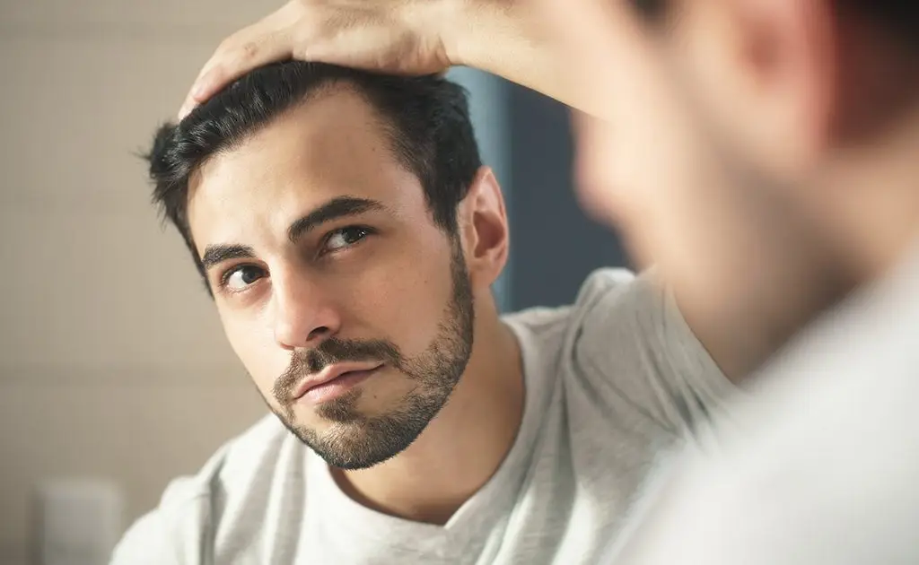 A person is looking into the mirror with a concerning look in his face about the hair loss signs with receding hairline.