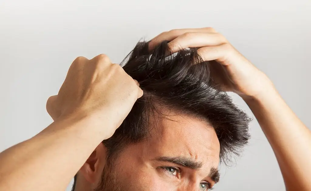A person is holding their hair up, worried and facing scalp problems.