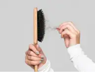 The image shows a person pulling tangled hair from a wooden hairbrush with black bristles. Has hair fall problems.